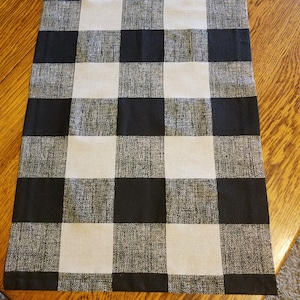 May include: Black and white checkered table runner. The runner is made of a woven fabric with a subtle texture.