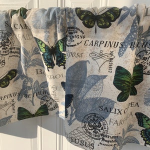 May include: A cream-colored fabric with a blue and green butterfly pattern. The fabric has a vintage look with text and stamps that include the words "CARPINUS BLUS" and "SALIX C PEA".