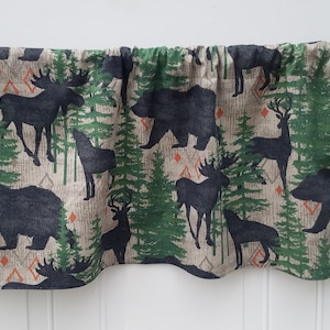 May include: A valance with a woodland theme featuring silhouettes of moose, bears, deer, and wolves on a beige background with green trees and orange diamond patterns.