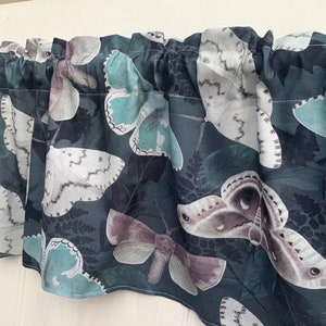 May include: A teal blue valance with a pattern of white, gray, and brown moths on a dark teal background.