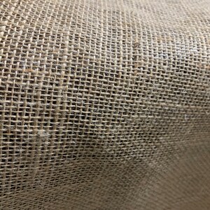 K&ouml;nnte beinhalten: Nahaufnahme eines nat&uuml;rlichen braunen Jutegewebes mit einer gewebten Textur. Der Stoff besteht aus Naturfasern und hat ein raues, rustikales Aussehen.