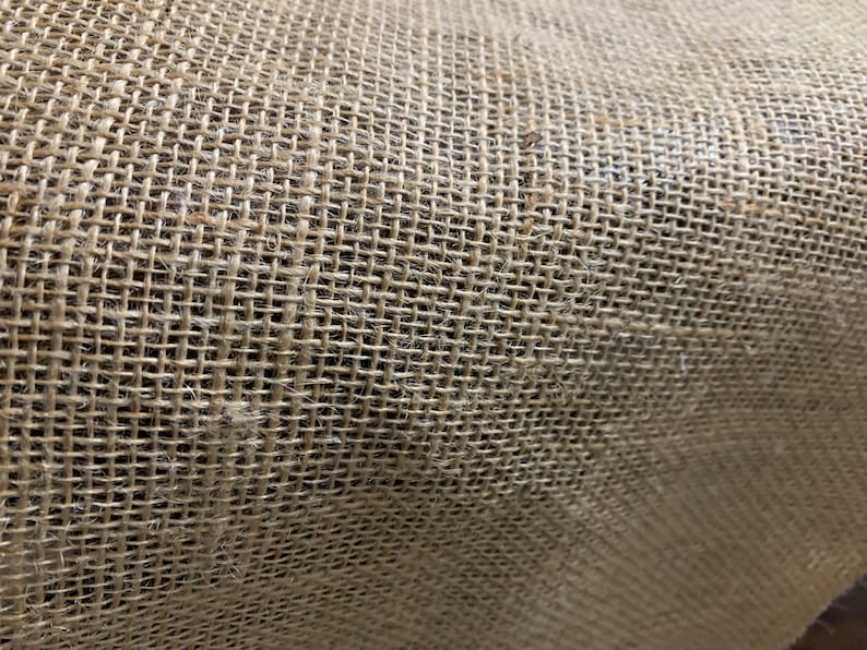 K&ouml;nnte beinhalten: Nahaufnahme eines nat&uuml;rlichen braunen Jutegewebes mit einer gewebten Textur. Der Stoff besteht aus Naturfasern und hat ein raues, rustikales Aussehen.