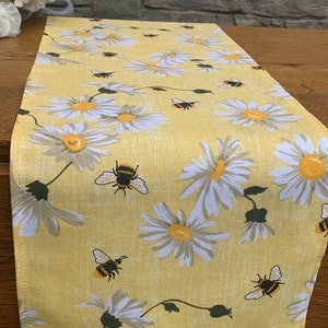 May include: A yellow table runner with a white daisy and bumblebee pattern.