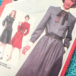 Peut inclure: Une pochette de patron de couture Simplicity pour une robe avec un tour de poitrine de 91,44 cm. La couverture présente des illustrations d'une robe à manches longues avec col, nœud papillon et ceinture. Le texte inclut Simplicity et BUST 36" COMPLETE DRESS.