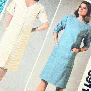 Pode incluir: Um envelope de molde de costura McCall's 8911 apresentando duas variações de vestido. Um é um vestido de riscas claras com botões frontais e o outro é um vestido azul liso de manga comprida com dois bolsos. Texto: BUST 32.5" CUT COMPLETE.