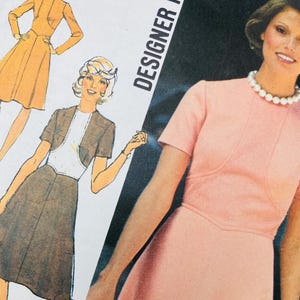 Może przedstawiać: Koperta z wykrojem krawieckim vintage przedstawiająca różową sukienkę z krótkim rękawem, wysokim dekoltem i białym naszyjnikiem z pereł. Ilustracja pokazuje dwa warianty sukienki, jeden z żakietem. Tekst zawiera DESIGNER oraz BUST 36" COMPLETE 1970S.