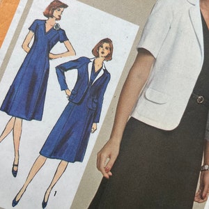 Può includere: Una busta per cartamodello Simplicity con illustrazioni e una fotografia di un completo a due pezzi. Il design include una giacca bianca a maniche corte con tasche e un abito scuro con scollo a V e una cintura sottile.