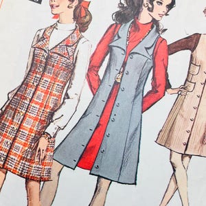 Op de afbeelding: Een vintage Simplicity naaipatroon-envelop met illustraties van drie mouwloze jurken gedragen over tops met lange mouwen. De ontwerpen omvatten een geruite jurk, een effen blauwe jurk met knoopsluiting en een beige jurk met opgestikte zakken.
