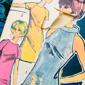 Może przedstawiać: Koperta z wykrojem krawieckim w stylu vintage zatytułowana Mandella, zawierająca ilustracje trzech różnych stylów sukienek. Koperta przedstawia żółtą sukienkę, różową sukienkę i niebieską sukienkę bez rękawów. Papierowa koperta jest w kilku miejscach podarta.