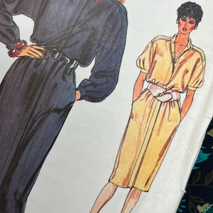 May include: A sewing pattern envelope labelled Easy Vogue featuring illustrations of two outfits. One is a dark navy long-sleeved dress with a white collar and belt. The other is a yellow short-sleeved dress with a white belt and button-down front.