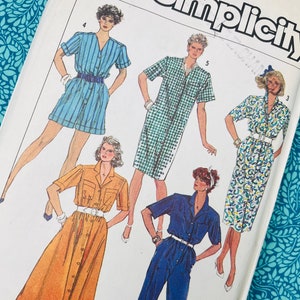 Puede incluir: Un sobre de patrón de costura Simplicity con ilustraciones de cinco estilos de ropa diferentes, incluyendo un romper a rayas azules, un vestido camisero a cuadros verdes, un vestido con estampado floral, un vestido amarillo mostaza y un mono azul.