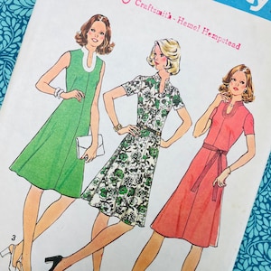 Könnte beinhalten: Ein Simplicity-Schnittmusterumschlag mit Illustrationen von drei Kleidern. Ein ärmelloses grünes Kleid mit weißem Kragen, ein kurzärmeliges weißes Kleid mit grünem Blumenmuster und ein kurzärmeliges korallenfarbenes Kleid mit Bindegürtel.