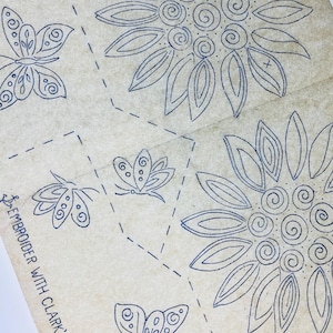 Könnte beinhalten: Ein Vintage-Transfermuster auf gealtertem Papier mit dunkelblauen Tintenumrissen von zwei großen Sonnenblumen und drei Schmetterlingen. Der Text lautet WOMAN CRAFT N°120 und EMBROIDER WITH CLARK'S ANCHORT, ergänzt durch gestrichelte Linien.