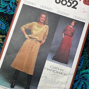Può includere: Cartamodello vintage Simplicity 8652 con una donna in un abito beige e una donna in un abito bordeaux. Il modello è taglia 12, busto 87 cm. Il modello include il nome della stilista, Cathy Hardwick.