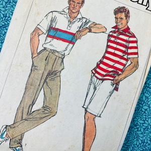 May include: Vintage Simplicity sewing pattern featuring illustrations of two men in polo shirts and shorts. One man wears a white polo with blue and red stripes, the other wears a red and white striped polo. The pattern is on a cream-colored background.