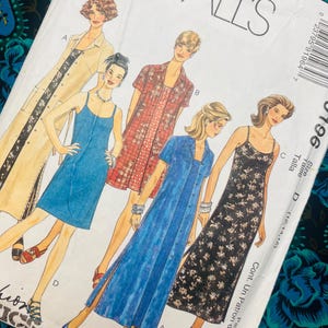 May include: A McCall's sewing pattern envelope featuring illustrations of four different dress styles labeled A, B, C, and D. The designs include a long beige coat-style dress, a short red patterned dress, a blue button-front dress, and a black floral dress.