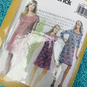 May include: A Butterick sewing pattern packet, B5812, featuring illustrations of three different dresses. The packet is sealed in clear plastic and includes the CraftsWoman Fabrics address and contact information. The dresses are in pink, purple, and blue.