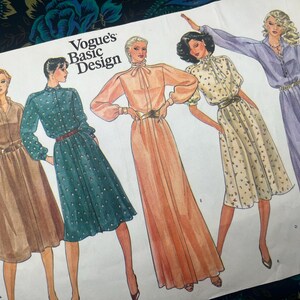 May include: A Vogue's Basic Design sewing pattern envelope illustration featuring five different dress styles. The drawings display various silhouettes including midi and floor-length dresses with long sleeves, high collars, and waist belts in shades of brown, teal, peach, cream, and purple.