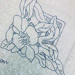 May include: A floral embroidery pattern in navy blue on a light background. The design features a large flower with multiple petals and leaves, enclosed in a geometric shape. The words "OLD BLEACH" are visible.