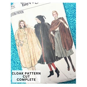 Può includere: Un modello di cucito vintage per mantelli. L'illustrazione mostra tre diversi modelli di mantello in vari colori, tra cui beige, nero e marrone. Il testo "CLOAK PATTERN CUT COMPLETE" è visibile nella parte inferiore del modello.