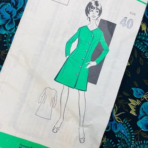Op de afbeelding: Een vintage naaipatroon-envelop met nummer 420, maat 40, met een groene illustratie van een jurk met lange mouwen, een V-hals en een knoopsluiting aan de voorzijde. De envelop bevat een schets van de achterkant en het adres 79 Camden Road, London.