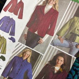 May include: A sewing pattern envelope featuring illustrations and photographs of various jacket styles. The designs include a red blazer, a green jacket with a tie belt, a purple jacket with pleats, and a dark maroon jacket with a decorative collar.