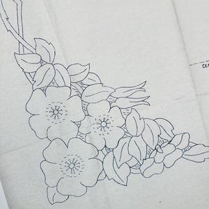 Könnte beinhalten: Ein Schnittmusterteil aus cremefarbenem Seidenpapier mit einer dunkelblauen Strichzeichnung eines Blumenarrangements aus mehreren Blüten, Knospen und Blättern. Der Text CE ist auf der rechten Seite des Papiers teilweise sichtbar.