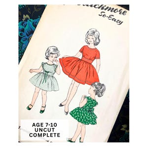 Op de afbeelding: Vintage naaipatroon met illustraties van meisjes in jurken. Het patroon heeft de tekst "Buckmore So-Easy" en "AGE 7-10 UNCUT COMPLETE". De jurken zijn rood en groen met witte stippen.