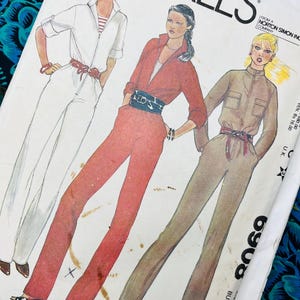 以下が含まれることがあります： ヴィンテージのマッコールズの裁縫パターン封筒。3人の女性がジャンプスーツを着ているイラストが描かれています。ジャンプスーツは白、赤、タン色です。封筒にはMcCall'sのロゴとパターン番号6908が記載されています。