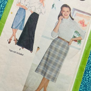 Może przedstawiać: Koperta z wykrojem krawieckim Simplicity 9070 z ilustracjami trzech fasonów spódnic. Widoczna jest niebieska spódnica do kolan, długa czarna spódnica oraz spódnica w kratę. Tekst zawiera napis Simplicity 9070 oraz Tops not included.