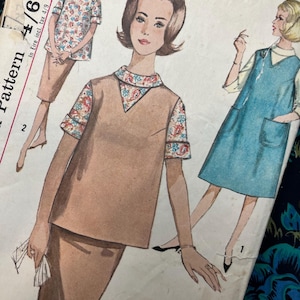 Può includere: Una busta di cartamodello vintage con illustrazioni di due completi: un set gonna e top color marrone chiaro con colletto e polsini a motivo paisley, e un abito senza maniche blu indossato sopra un top chiaro. Il testo include Maternity Size 14 Bust 34.