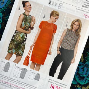 Peut inclure: Un patron de couture Burda Style avec trois modèles de robes. Le patron présente des images des vêtements finis : une robe sans manches à motifs, une robe orange à manches courtes et un haut à motifs avec un pantalon noir. Le numéro du patron est 6914.