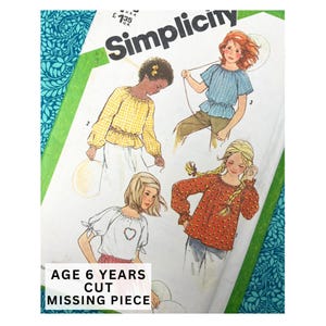 May include: Vintage Simplicity sewing pattern for girls' tops. The pattern features illustrations of four different top designs. The text on the pattern reads "AGE 6 YEARS CUT MISSING PIECE". The background has a teal floral design.