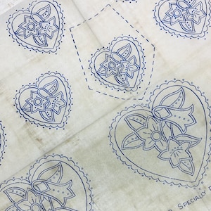 May include: Off-white fabric featuring a repeating pattern of blue heart-shaped floral designs. Each heart contains a flower and leaf motif, outlined with a dotted border. The fabric appears to be vintage or aged.