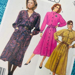 May include: Vintage McCall's sewing pattern featuring three dress designs. The dresses are shown in paisley, pink, and mustard yellow. The pattern includes long sleeves, button-down fronts, and belted waists. The pattern is on a white background.