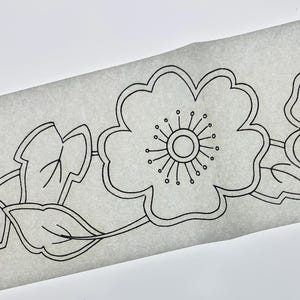 Könnte beinhalten: Eine schwarze Strichzeichnung auf durchscheinendem weißem Papier mit einem sich wiederholenden Blumenmuster. Das Design besteht aus stilisierten fünfblättrigen Blüten mit kreisförmigen Zentren und strahlenden Staubgefäßen sowie spitzen Blättern.