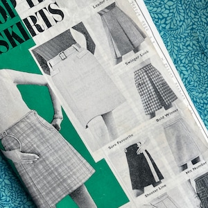 May include: A vintage sewing pattern titled "Top Ten Skirts" with illustrations of different skirt designs. The pattern is printed in black and white with green highlights. The image is set against a patterned blue background.
