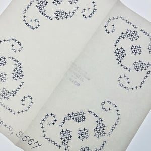 May include: A white paper sheet featuring three repeating dark blue cross-stitch patterns of stylised floral or paisley shapes. The paper includes the printed text "9567" and "TURKEY" in blue ink, with visible fold lines across the surface of the paper.