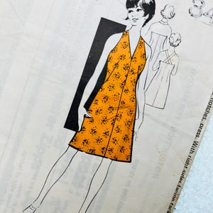 May include: A vintage sewing pattern envelope featuring a line drawing of a sleeveless dress with a V-neckline and a knee-length hem. The dress is colored in bright orange with a small black floral print. The text 460 and 34 are visible.