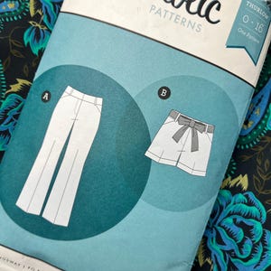 Op de afbeelding: Een Sewaholic Patterns envelop voor het Thurlow-ontwerp, maten 0-16. De lichtblauwe verpakking bevat twee illustraties: A toont een lange broek met een tailleband, en B toont een korte broek met een strikceintuur. De tekst bevat de merknaam.
