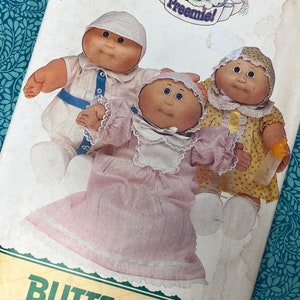 May include: A vintage Butterick pattern featuring three Cabbage Patch Kids Preemies dolls. The dolls are dressed in pastel-coloured outfits, including a pink dress, a yellow dress, and a white outfit with blue accents. The pattern is on a white background with green text.