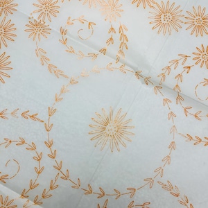 May include: White fabric featuring a repeating pattern of orange flowers and leafy vines. The floral design is evenly spaced across the fabric, creating a delicate and decorative look. The fabric appears to be thin and lightweight.