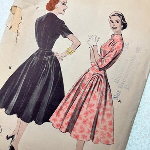 以下が含まれることがあります： 2 人の女性がドレスを着ているイラストが描かれた、ヴィンテージの裁縫パターン。一人は黒、もう一人はピンクの花柄。パターンはサイズ 30 で、「RN」の文字が含まれています。