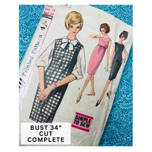 May include: A vintage sewing pattern envelope for a dress, featuring illustrations of three different dress styles. The text includes Teen Size 14, Bust 34, Simple to Sew, and Bust 34" Cut Complete. The envelope is white with black and pink text.