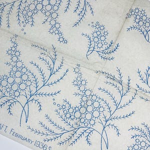 Op de afbeelding: Een lichtbeige stof met een herhalend blauw inktpatroon van mimosatakjes en bladeren. De tekst STITCHCRAFT, FEBRUARY 1936 is in blauwe inkt gedrukt in de linkerbenedenhoek. De stof vertoont zichtbare vouwlijnen over het oppervlak.