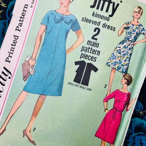 Può includere: Una busta per cartamodello vintage per un abito Jiffy con maniche a kimono, che mostra illustrazioni di tre varianti di abito in blu tinta unita, stampa floreale e rosa tinta unita. Il testo include Jiffy, kimono sleeved dress e 2 main pattern pieces.