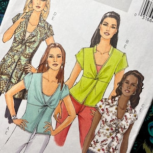 May include: A Butterick sewing pattern envelope featuring illustrations of four different tops. The designs include a long patterned tunic, a solid light blue top, a solid lime green top, and a white top with a red and brown floral print.