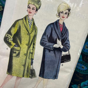 Könnte beinhalten: Vintage Schnittmuster mit Illustrationen von zwei Frauen in langen Mänteln. Ein Mantel ist olivgrün, der andere marineblau. Das Muster enthält den Text "PRINT" und Größenangaben. Die Frauen tragen Handschuhe, Handtaschen und Absätze.