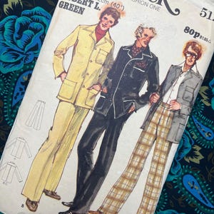 May include: Vintage Butterick sewing pattern featuring illustrations of three men's suits. The pattern includes a yellow suit, a black suit, and a gray suit with plaid pants. The text on the pattern reads "Butterick THE FASHION ONE" and "ROBERT L. GREEN".