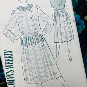 Op de afbeelding: Een naaipatroon-envelop met een groene lijntekening van een tweedelige outfit bestaande uit een geruit jasje met een ruchekraag en een bijpassende plooirok. De tekst WOMAN'S WEEKLY staat verticaal in het zwart aan de linkerzijde gedrukt.